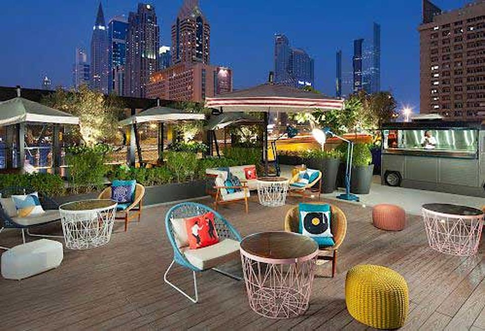 A rooftop lounge at dusk with lit towers behind it